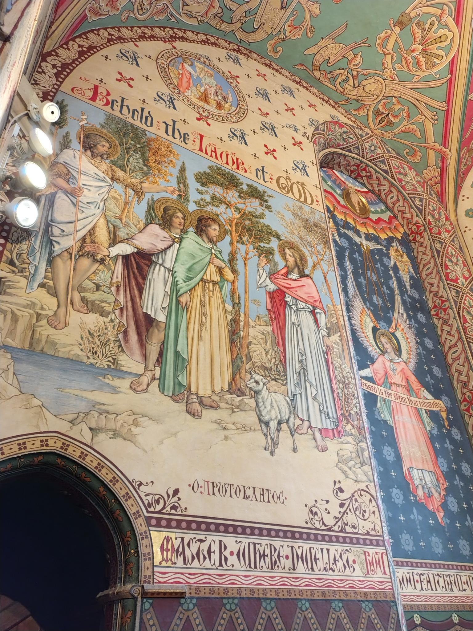 Gloucester Chapel A highly detailed, colourful mural in a Gloucester Cathedral chapel depicting biblical scenes, an angel, and the stylized text 'Behold the Lamb of God'.